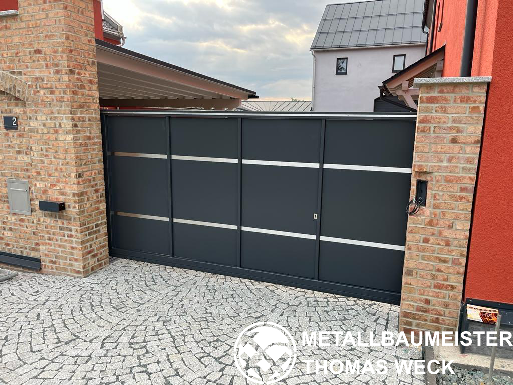 Schiebetor in Anthrazit mit waagerechten Edelstahl-Zierstreifen zwischen gemauerten Klinkerpfeilern